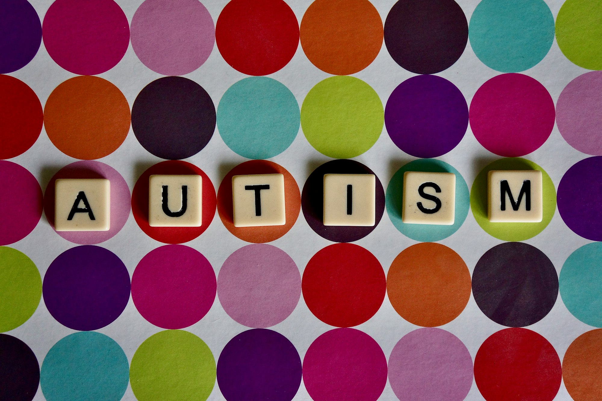 Scrabble letters spelling Autism on a multi-coloured polka dot background